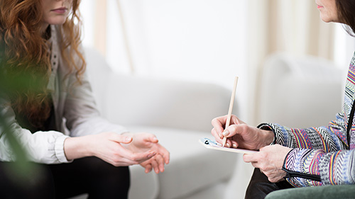 Applied Psychology student writing notes during a therapy session