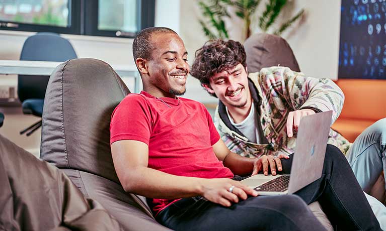 Two students sat on bean bags looking at a laptop