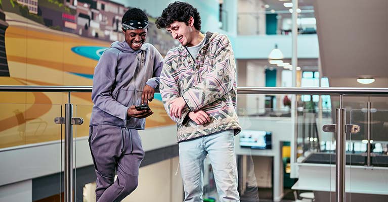 Two students leaning against a balcony looking at a phone