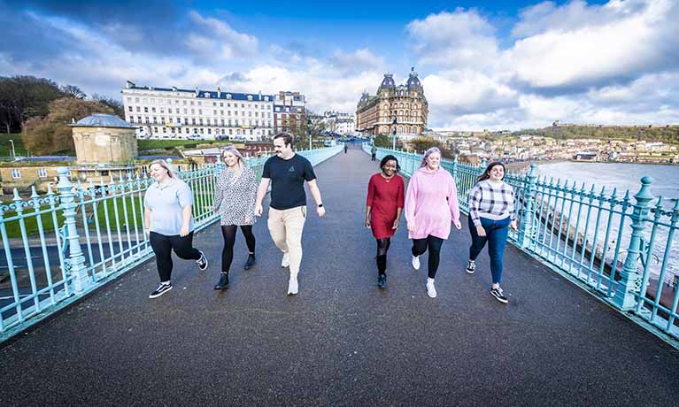 Group of people walking over a bridge overlooking the coast