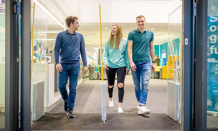 Three students talking whilst walking out of a building