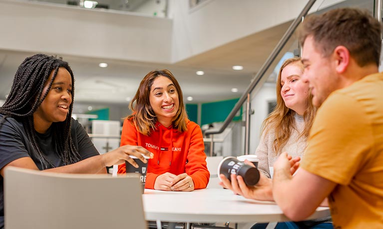 Four students smiling as they're sitting around a table.