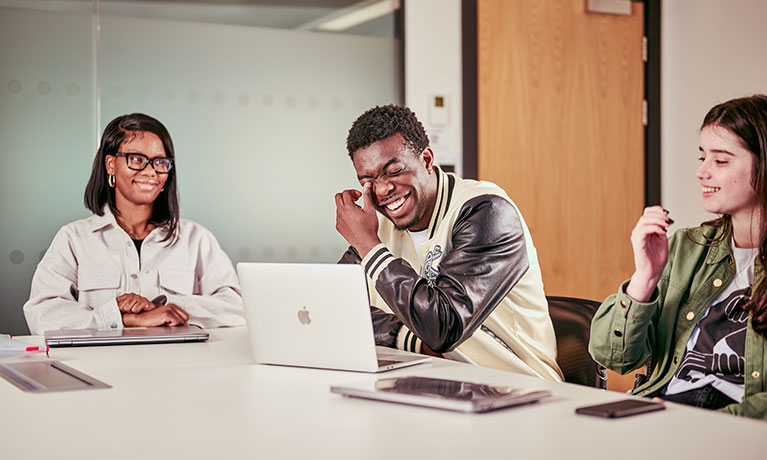 Three students sat at a table laughing and joking