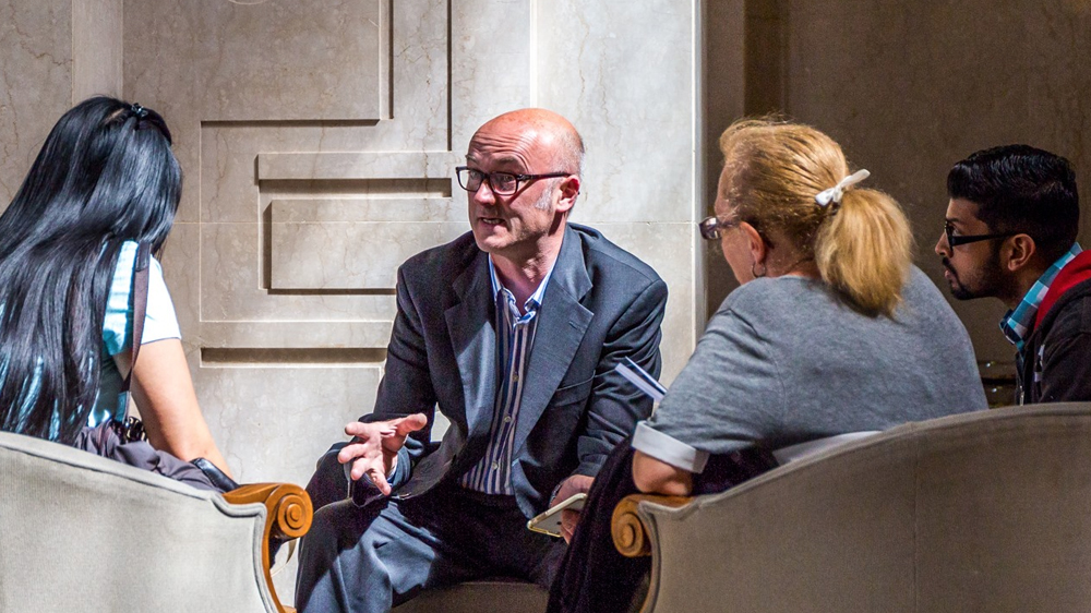 A male teacher sat in front of three adult students and talking