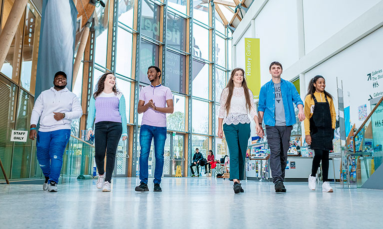 Students walking into the CU hub building on a bright day.