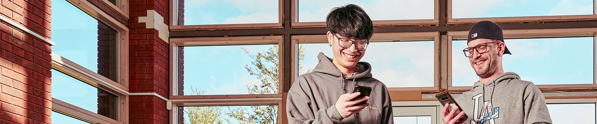 Two students stood inside looking at their mobile phones
