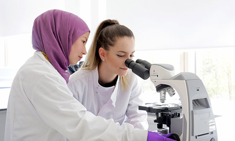 Two students wearing lab coats looking into a microscope