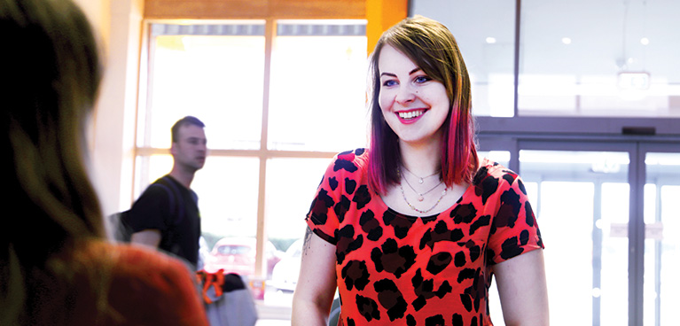 A student smiling while stood at the reception desk in the Mile Lane building.