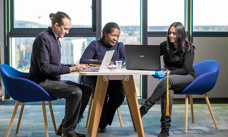 Two students sat around a table with a lecturer looking at their laptops