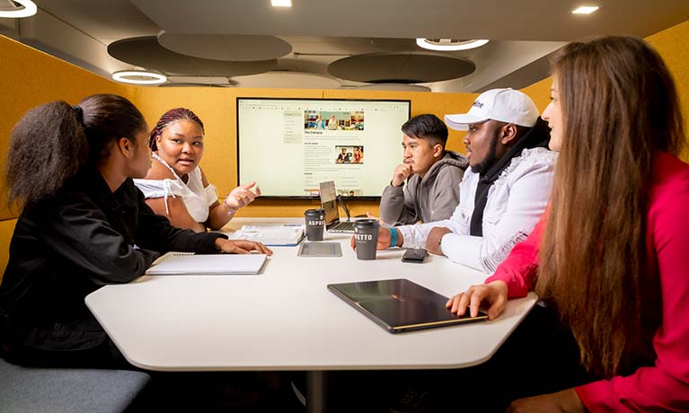 Group of students sat around a screen talking