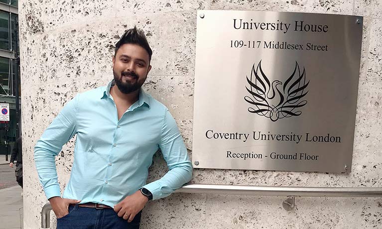 student Sabari Sulochanan Nair Madhuri standing at a Coventry University London wall plaque