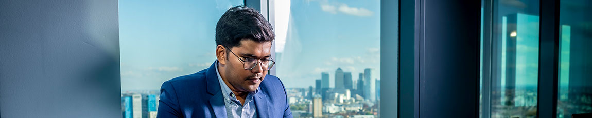 Male student sat in front of a window looking down towards a laptop