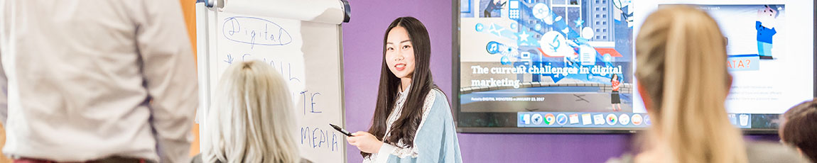 lady presenting to a group using a flip chart and presentation on screen