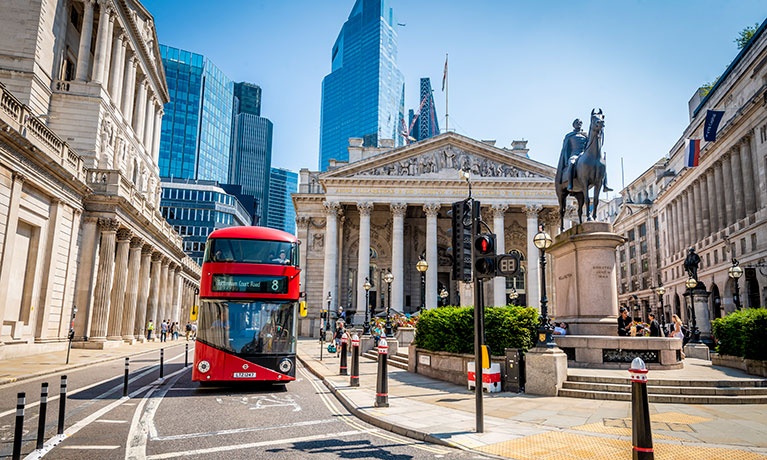 An image of a London street with a red bus driving down the middle.