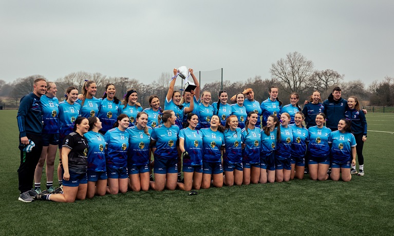 Coventry University Ladies Gaelic Football lined up celebrating their victory with the captain holding the trophy aloft