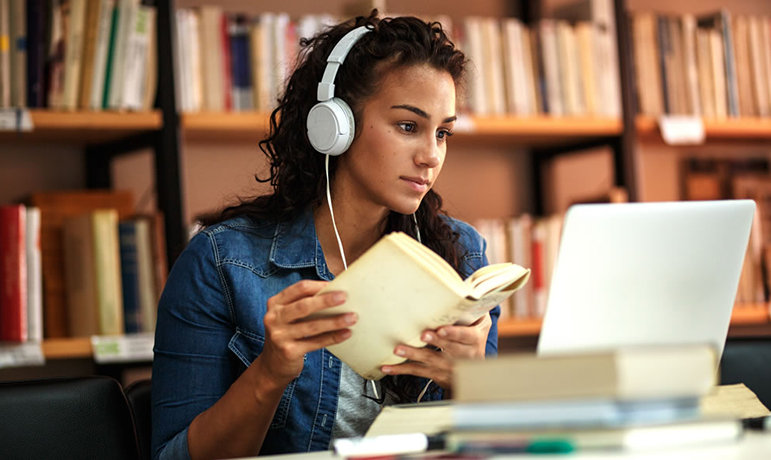 Female sat at a desk with headphones on looking at a laptop