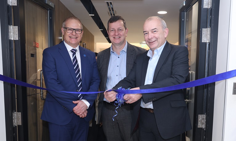 Three men cutting a ribbon in the doorway of a building