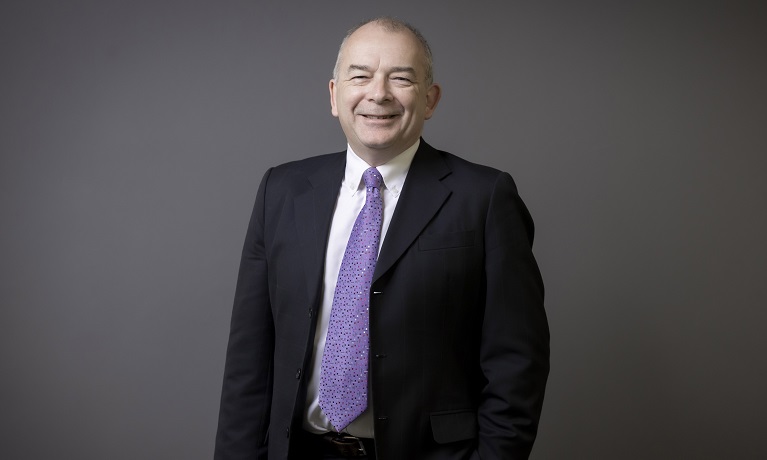Professor John Latham CBE in a dark suit, white shirt and purple tie