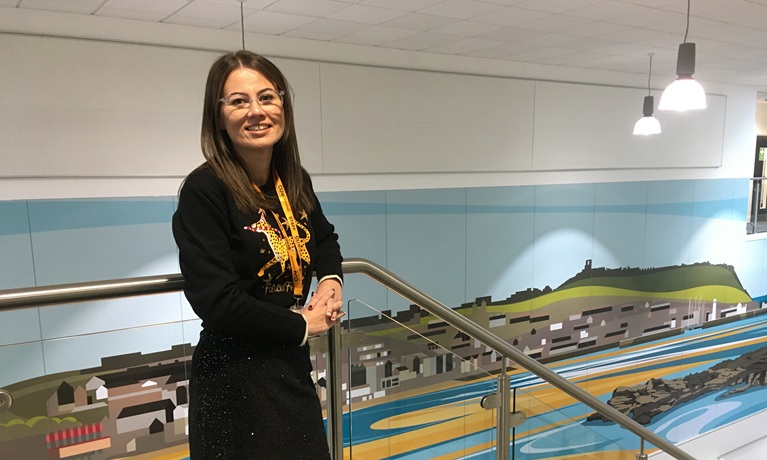 Sophie Pickard in the CU Scarborough building, leaning on a bannister smiling at the camera