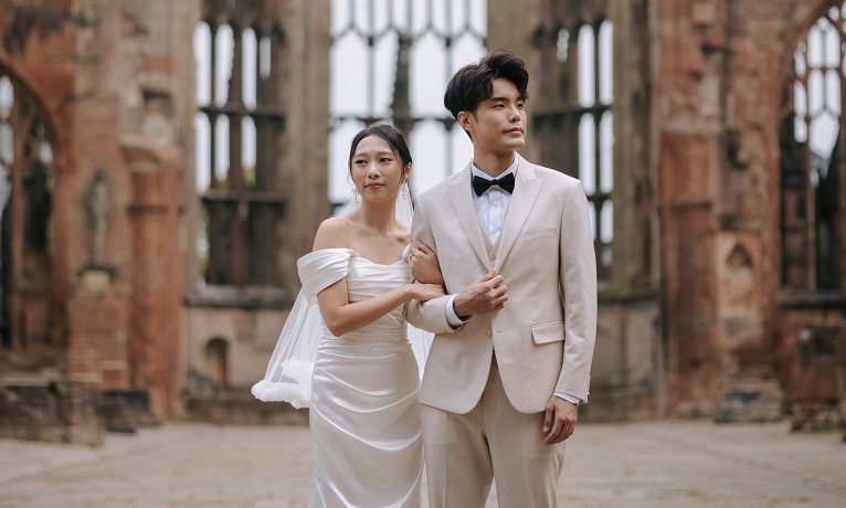 Jamie and Jason Ho wearing engagement celebration clothes while stood in the ruins of Coventry Cathedral