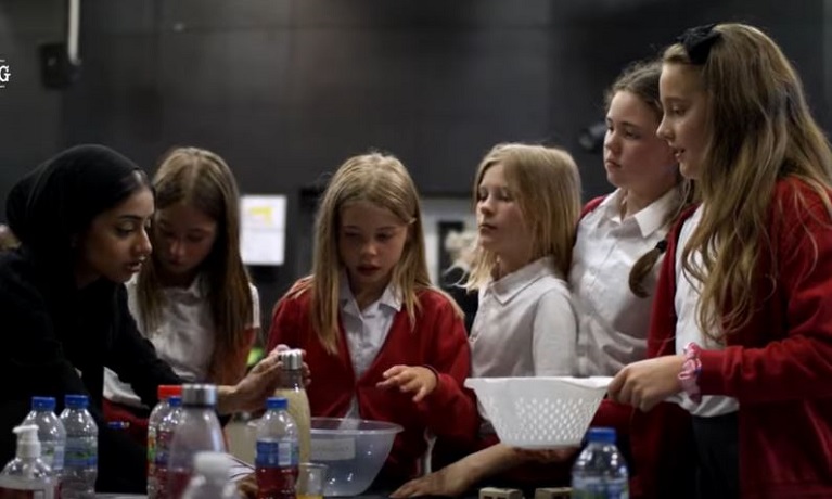 A group of five schoolgirls next to a table covered in bottles of liquids and mixing bowls