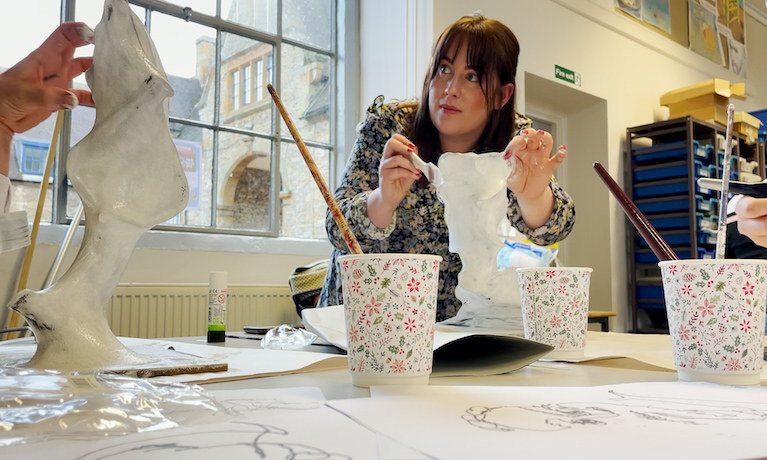 Young woman painting a miniature sculpture with white paint