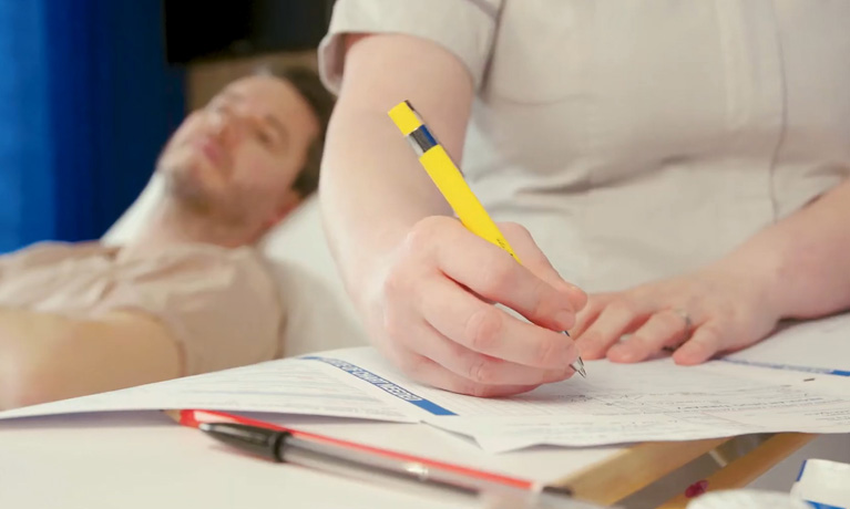 Close up of a nurse taking patient observations with patient lying in on a bed in the background