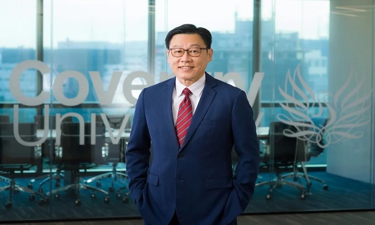 A man in a suit standing in front of a Coventry University logo