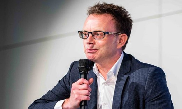 A man sitting on a stage speaking into a microphone