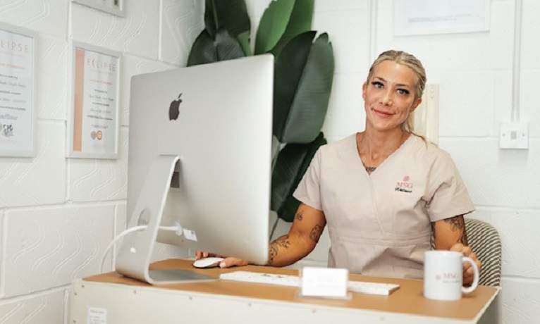 Maria Guedes looking at the camera while sat a desk with a computer on it
