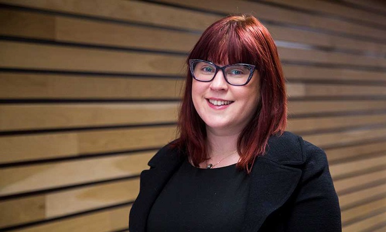 Dr Sally Pezaro pictured against a wood panelled background, wearing a black top and smiling at the camera.