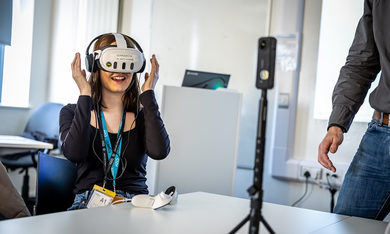 A female student sat at a table wearing a virtual reality headset and smiling