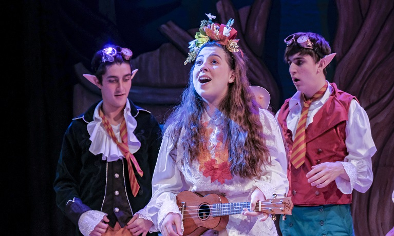 A female actor on stage with two male actors in the background