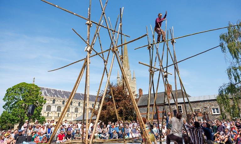 A performer balancing on a large bamboo construction in front of a large crowd watching on