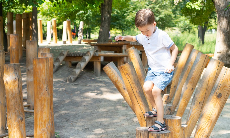 A young boy in t-shirt and shorts on wooden steps on a play area