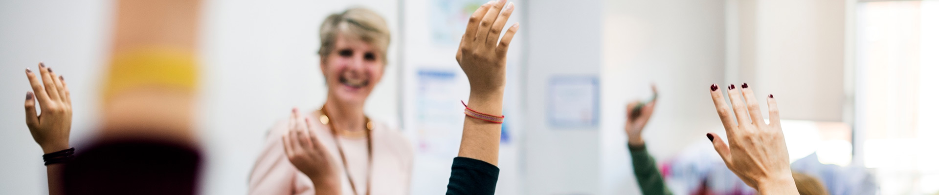 Teacher standing at the front of the classroom with students arms in the air