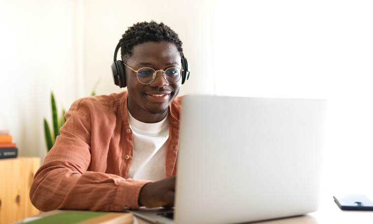 A man sat at a table wearing headphones with an open laptop in front of him