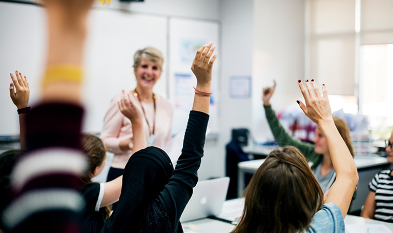 A teacher with students raising their hands