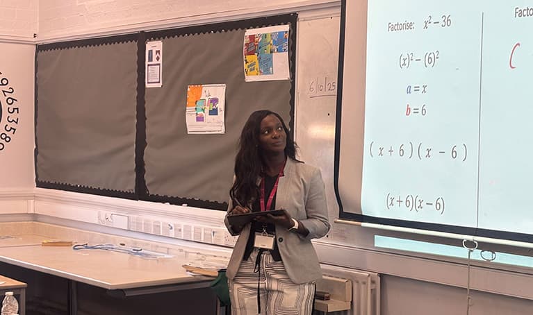 Haddy Jeng standing in front of a whiteboard with algebra looking at the screen