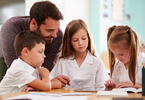 A teacher helping young schoolchildren with their reading.