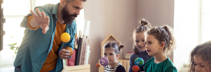 A male teacher with three students, each holding a model of a planet in the solar system.