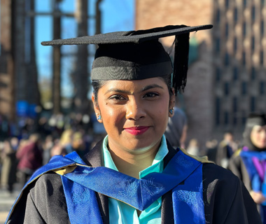 Angela Fernando wearing a graduation cap and gown, smiling at the camera at her graduation ceremony.