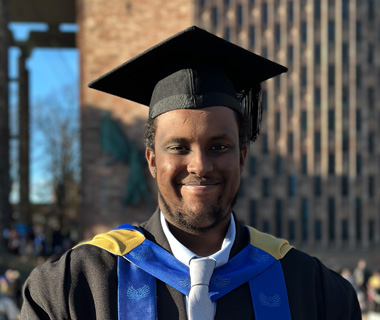 Ayub Faisal Elmi at his graduation ceremony, smiling and wearing a graduation cap and gown.