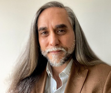 Portrait of David Mendez wearing a shirt and brown jacket against a white background.