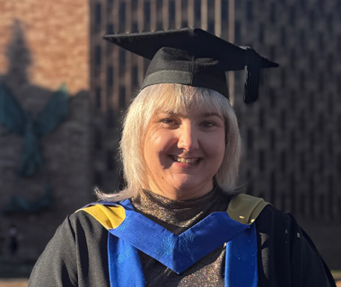 Jayne McFadden smiling in front of Coventry Cathedral at her graduation ceremony.