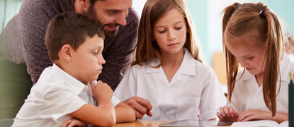 A teacher helping young schoolchildren with their reading
