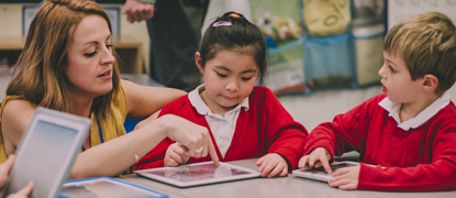 A teacher helping a young primary-aged child use a tablet