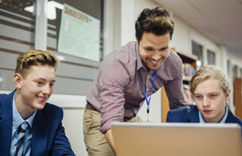 A male teacher helping a student using a laptop.