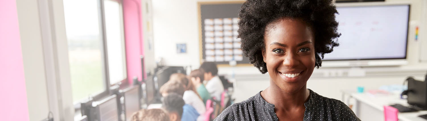 Close up of a woman smiling with children on computers in the background