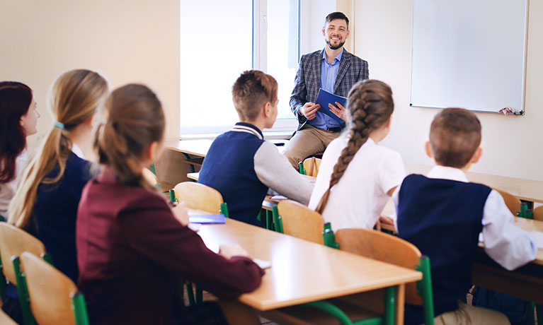 A teacher stood by a whiteboard in front of a class.